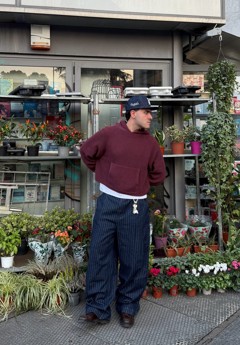 Burgundy cropped sweater and navy pinstriped wide-leg pants, complemented by a black cap and decorative keychain, against a floral background.