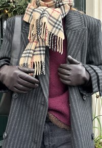 Schwarzer Nadelstreifenmantel, kastanienbrauner Pullover, beiger Kar scarf mit Fransen und braunen Lederhandschuhen. Dunkle Jeans am Bund sichtbar.