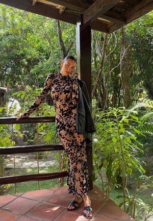 Vestido de manga larga ajustado en beige claro con manchas abstractas negras; combinado con una chaqueta de cuero negra y sandalias negras.