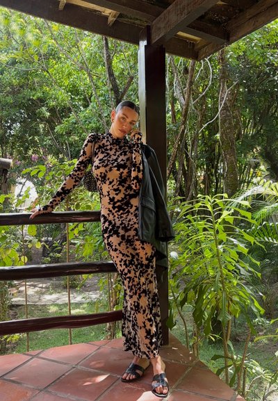 Vestido de manga larga ajustado en beige claro con manchas abstractas negras; combinado con una chaqueta de cuero negra y sandalias negras.