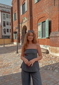 Γκρι strapless τοπ σε συνδυασμό με φαρδιά γκρι παντελόνια, με φόντο κόκκινα τούβλινα κτίρια και πλακόστρωτο δρό�μο.