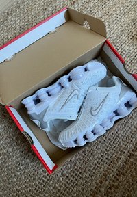 Λευκά Nike παπούτσια με υφή στην επιφάνεια και ορατό σύστημα αμορτισέρ. Συσκευασμένα σε ένα απλό χαρτόνι κουτί με κόκκινες λεπτομέρειες.