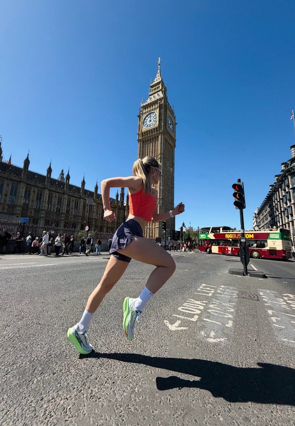 Nő sportos ruházatban fut a londoni Big Ben óratorony mellett egy napos napon, forgalommal és gyalogosokkal a közelben.