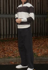 Quarter-zip pullover i svart og hvite striper, bomullsblanding, med høy krage og ribbet kant; kombinert med løse svarte jeans og hvite joggesko.