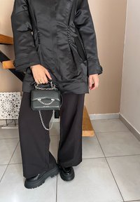 Μαύρο σατέν μπουφάν με κουμπιά στο πλάι, συνδυασμένο με φαρδιά μαύρα παντελόνια. Τα αξεσουάρ περιλαμβάνουν μια μικρή μαύρη τσάντα με ασημένια αλυσίδα. Χοντρές μαύρες παπούτσες.