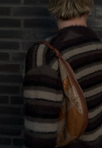 Sac à bandoulière en cuir marron avec un mélange de matériaux à motifs, présentant une forme courbée et une surface texturée, porté sur un pull rayé.