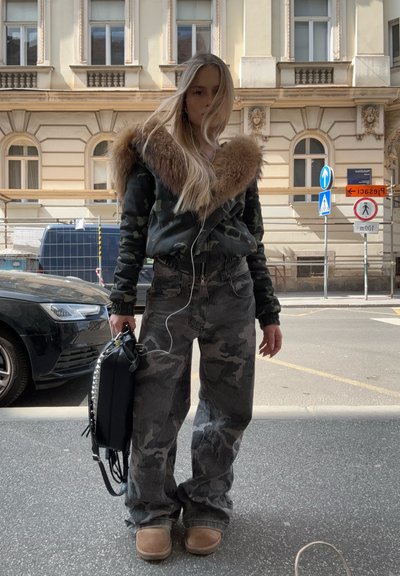 Chaqueta bomber de camuflaje con cuello de piel sintética, bolso negro con acentos de tachuelas, jeans holgados de patrón de camuflaje y zapatillas de felpa marrón claro.