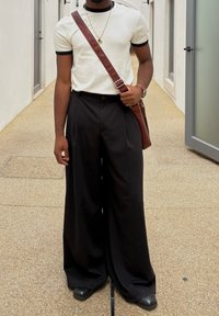 Hvit t-skjorte med korte ermer og svart kant, sammen med løstsittende svarte bukser. Brun crossover-sekk og svarte sko.