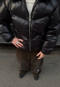 Black padded jacket with a zip front and triangular quilting design. Paired with loose brown trousers and multiple silver rings.