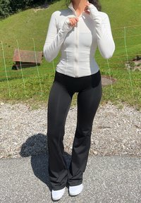 Haut à manches longues blanc zippé, pantalon noir ajusté et baskets blanches. Tissu lisse avec une légère brillance et orifices pour les pouces sur les manches.