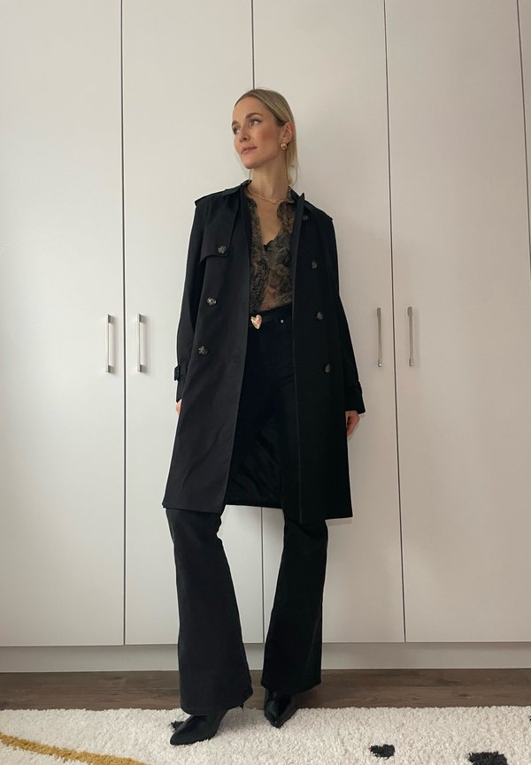 Trench coat negru, cu două rânduri de nasturi, completat cu un top din dantelă semi-transparentă, pantaloni negri cu talie înaltă și tocuri negre ascuțite.