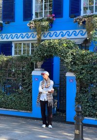 Bright blue building with white window frames and dark blue shutters. Ivy-covered entrance arches, decorative planters, and a cobblestone pathway.