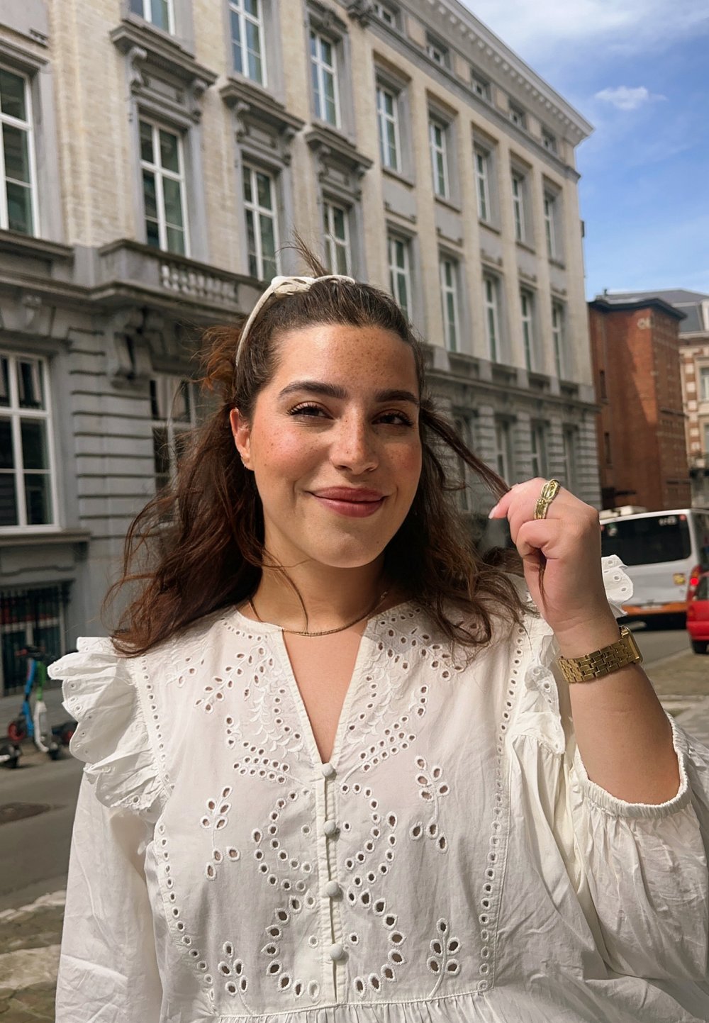 Λευκό κεντημένο φόρεμα με ρανίδες μανίκια, λεπτομέρειες από κουμπιά και σχέδια κοπής; φορεμένο με ένα χρυσό ρολόι και κορδέλα μαλλιών.