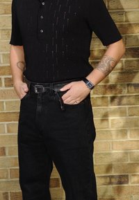 Μαύρη ριμπ κοντομάνικη πόλο μπλούζα με κουμπιά, με κατακόρυφες ρίγες. Συνδυασμένη με μαύρα ψηλόμεσα τζιν και μια μαύρη ζώνη.