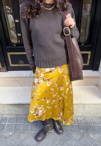 Pruun soonilise mustriga kampsun, kollase lillemustriga satiinseelik, pruun nahast kott ja põlveni ulatuvad pruunid saapad. Seelikul on detailne lillemuster ja sile kangas.