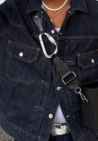 Veste en denim bleu foncé avec deux poches poitrine, boutons argentés et couture orange. Dotée d'une sangle noire et d'un attache carabine.