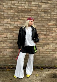 Svart lærjakke, hvit oversized t-skjorte, svart skjørt med grønne striper, løse hvite bukser, gule sko, rutet hårbånd, sølvkjede.