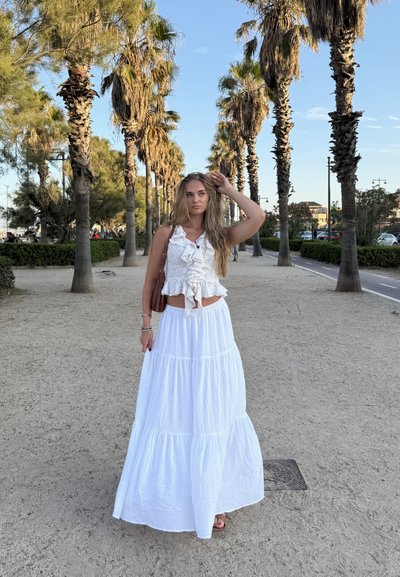 Falda maxi blanca con capas en volantes y una parte superior arrugada texturizada. El conjunto presenta un diseño envolvente y se combina con un bolso marrón.