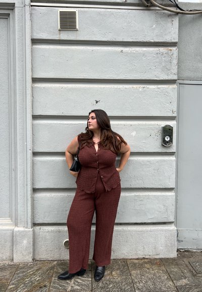 Conjunto de chaleco texturizado en color óxido y pantalones de pierna ancha con bordes en forma de onda; acompañado de un pequeño bolso negro y botas de tobillo.