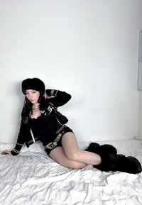 Chapeau en fausse fourrure noire, veste zippée noire avec accents blancs, débardeur noir et short. Bottes épaisses en fourrure noire. Bijoux argentés et petit sac.