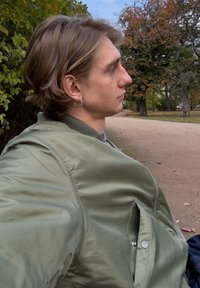 Õlivärvi rohelisest läikivast materjalist bomberjakk, millel on ees tõmblukk ja küljetasku. Loomulik keskkond puude taustal.