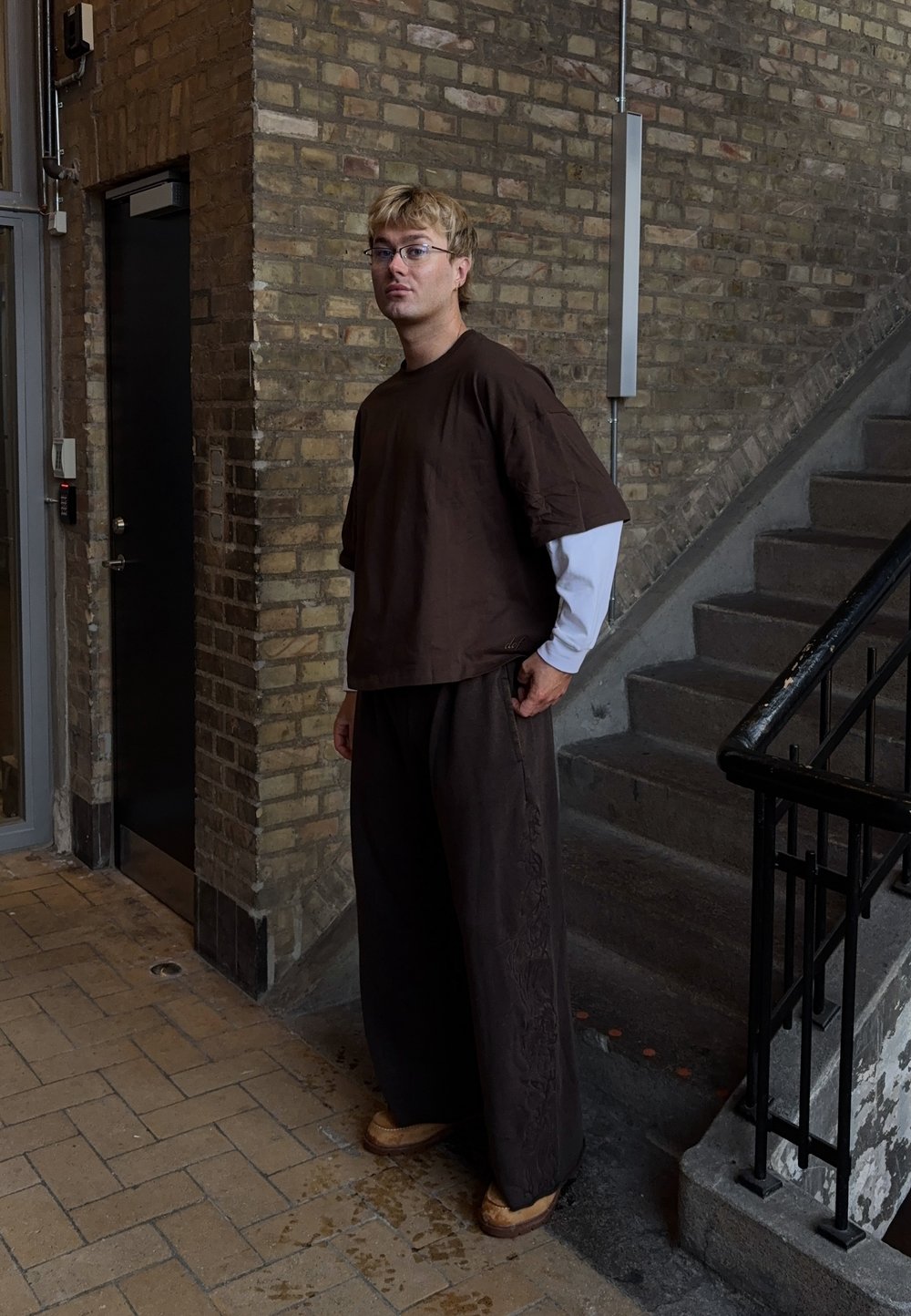 Haut ample marron et pantalon large assorti avec des accents texturés. Chemise blanche à manches longues en dessous. Sabots en bois aux pieds.