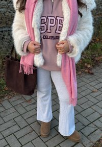 Borsa tote in suede marrone, sciarpa rosa con frange, felpa grigia in pile con stampa "SPE", pantaloni della tuta grigi e stivali alla caviglia color cuoio. Cappotto bianco con rifiniture in pelliccia.