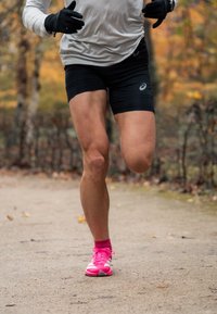 Jobb láb térd alatti amputált futó fekete rövidnadrágot és élénk rózsaszín cipőt viselve fut egy földúton őszi környezetben.