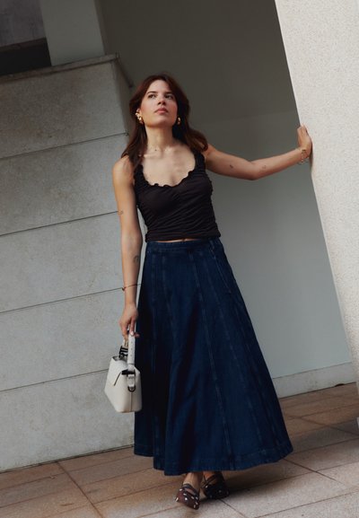 Top negro con fruncidos y falda larga de mezclilla oscura, combinados con un pequeño bolso blanco y tacones marrones con lunares blancos.