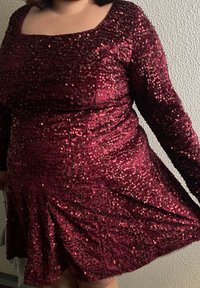 Robe bordeaux en sequins avec manches longues, encolure carrée et jupe évasée. Le tissu est brillant avec une apparence texturée due aux sequins.