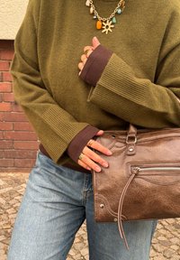 Pull en maille vert olive avec des poignets marron, assorti à un jean bleu clair. Sac à main marron texturé avec un détail zippé et des accents métalliques.