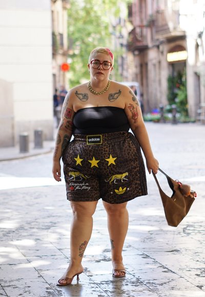 Top negro sin tirantes, pantalones cortos de estampado de leopardo con estrellas amarillas y leopardos, collar de cadena dorada, sosteniendo un bolso marrón, usando tacones transparentes.