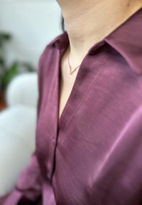 Chemise à manches longues couleur violet profond en tissu lisse avec un col en V. Présente un délicat collier en or rose avec un pendentif géométrique.