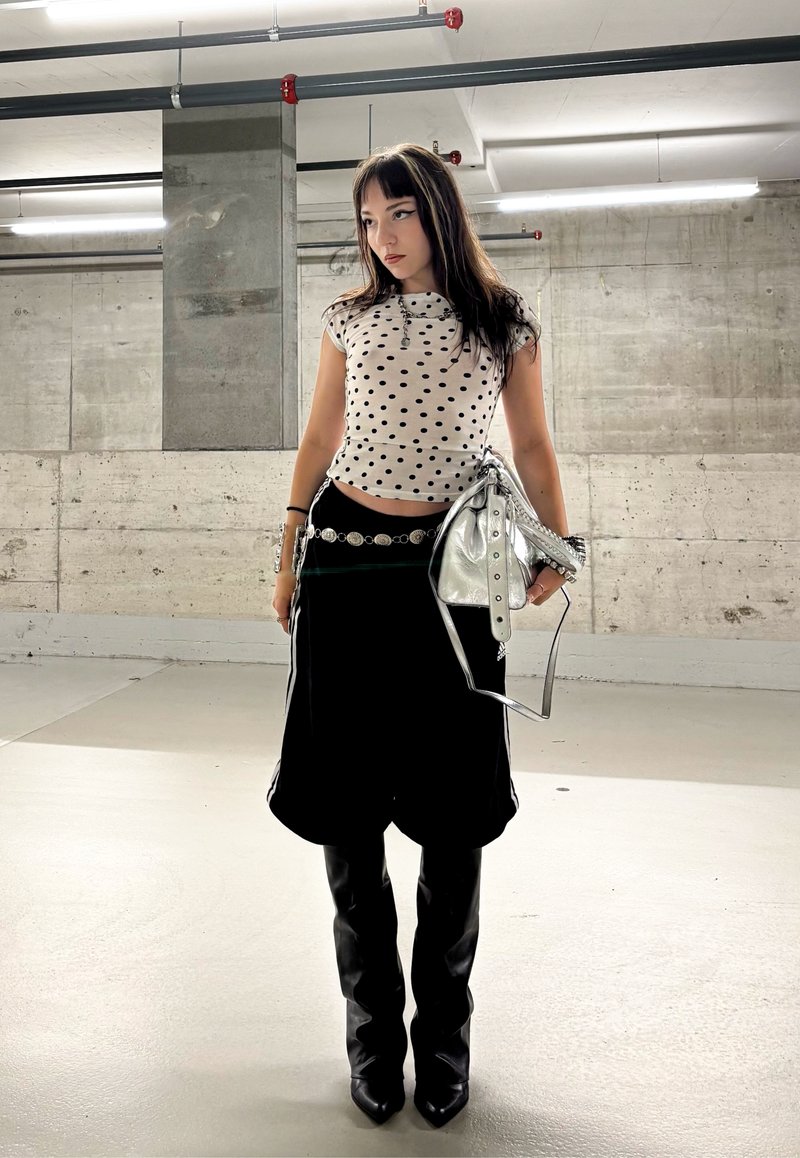 Shorts larges noirs associés à un haut ajusté à pois blancs, une ceinture argentée et un sac à main argenté brillant. Comprend des bottes noires montantes.