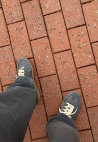 Pieds chaussés de baskets grises et pantalons foncés debout sur un pavé en briques rouges avec une texture visible et des interstices.