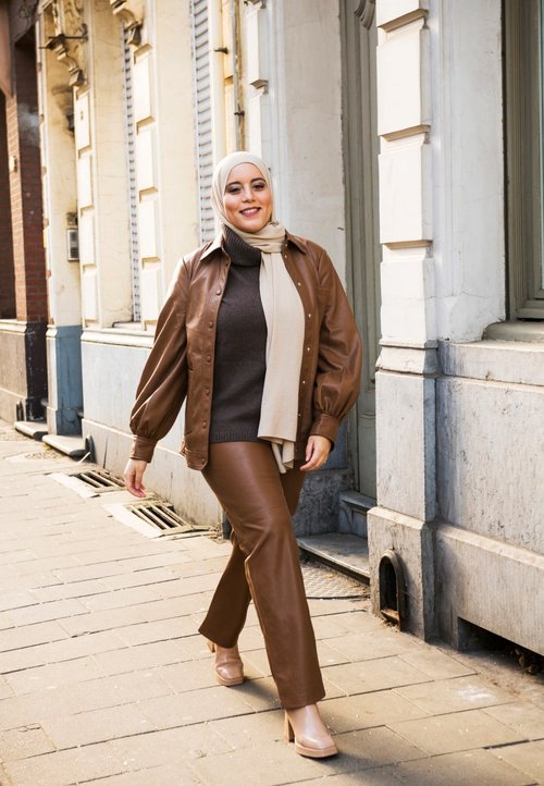 Light pink knitted vest over a white shirt, paired with brown wide-leg trousers. Features a white geometric handbag and beige shoes.