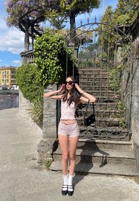 Δύο κομμάτια ρούχων με λευκό φόντο και κόκκινο λουλουδάτο σχέδιο. Το μοντέλο φοράει ένα εφαρμοστό τοπ και σορτς, συνδυασμένα με μαύρα γυαλιά ηλίου και κάλτσες, καθώς και χοντρά παπούτσια.