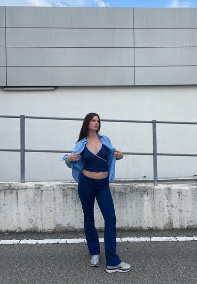 Conjunto atlético azul que incluye una parte superior ajustada y pantalones de talle alto, combinados con una camisa de botones azul claro. Zapatillas grises completan el conjunto.