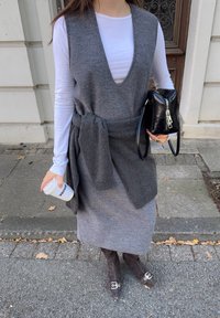 Rochie fără mâneci din amestec de lână gri, cu decolteu adânc în V și talie legată, purtată peste un top alb cu mâneci lungi, asortată cu cizme maro închis cu vârf ascuțit.