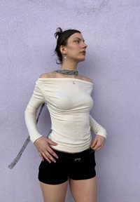 Top crema cu umerii descoperiți, cu mâneci lungi, dintr-un material texturat și o eșarfă gri la gât. Purtați cu pantaloni scurți negri și o curea.
