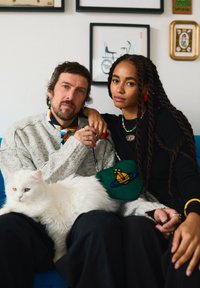 Homme et femme assis près l'un de l'autre sur un canapé bleu, la femme posant son bras sur l'épaule de l'homme, chat blanc sur les genoux de l'homme, œuvre encadrée en arrière-plan.