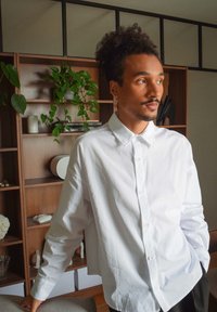 Vit skjorta med avslappnad passform och spetsig krage. Slät bomullstyg med synliga sömmar, bärs tillsammans med svarta byxor.