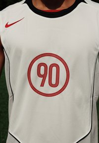 Biely športový dres s čiernymi akcentmi; uprostred sa nachádza okrúhly červený grafický symbol "90" a na ramene je malé červené logo Nike.
