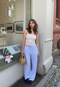 Λευκή τοπ χωρίς τιράντες με μικρά λουλουδάτα σχέδια, ανοιχτό μπλε παντελόνι με κάθετους ρίγες, καφέ τσάντα με κόμπους και μαύρα παπούτσια.