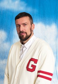 White cardigan featuring a red letter "G" and two red stripes on the sleeves, buttoned over a white collared shirt; crafted from textured knit material.