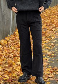 Melni svītraini zvērpji bikses ar gludu tekstūru. Jostasvieta ērti sedzas ap vidukli. Kombinētas ar melnām platformas kurpēm.