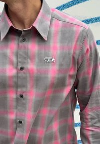 Hall roosa ruuduline särk, pikkade varrukatega, millel on nööpidega kaelus ja väike logo rinnal. Kangas tundub sile.