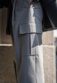 Grå avslappnade cargobyxor i texturerad tyg, med en sida ficka och skräddarsydd passform, kompletterad av en mörk blazer.