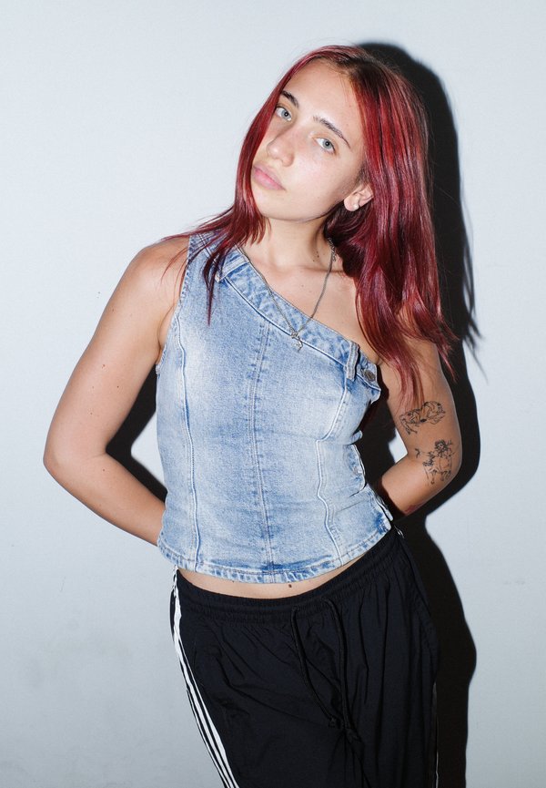 Top en denim court avec un design asymétrique, couleur bleu clair et détails de couture. Associé à un pantalon de sport noir avec des rayures blanches.