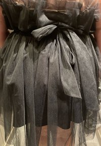 Robe en tulle noir avec tissu transparent à texture plissée et taille nouée. Design fluide et superposé avec un aspect doux et léger.